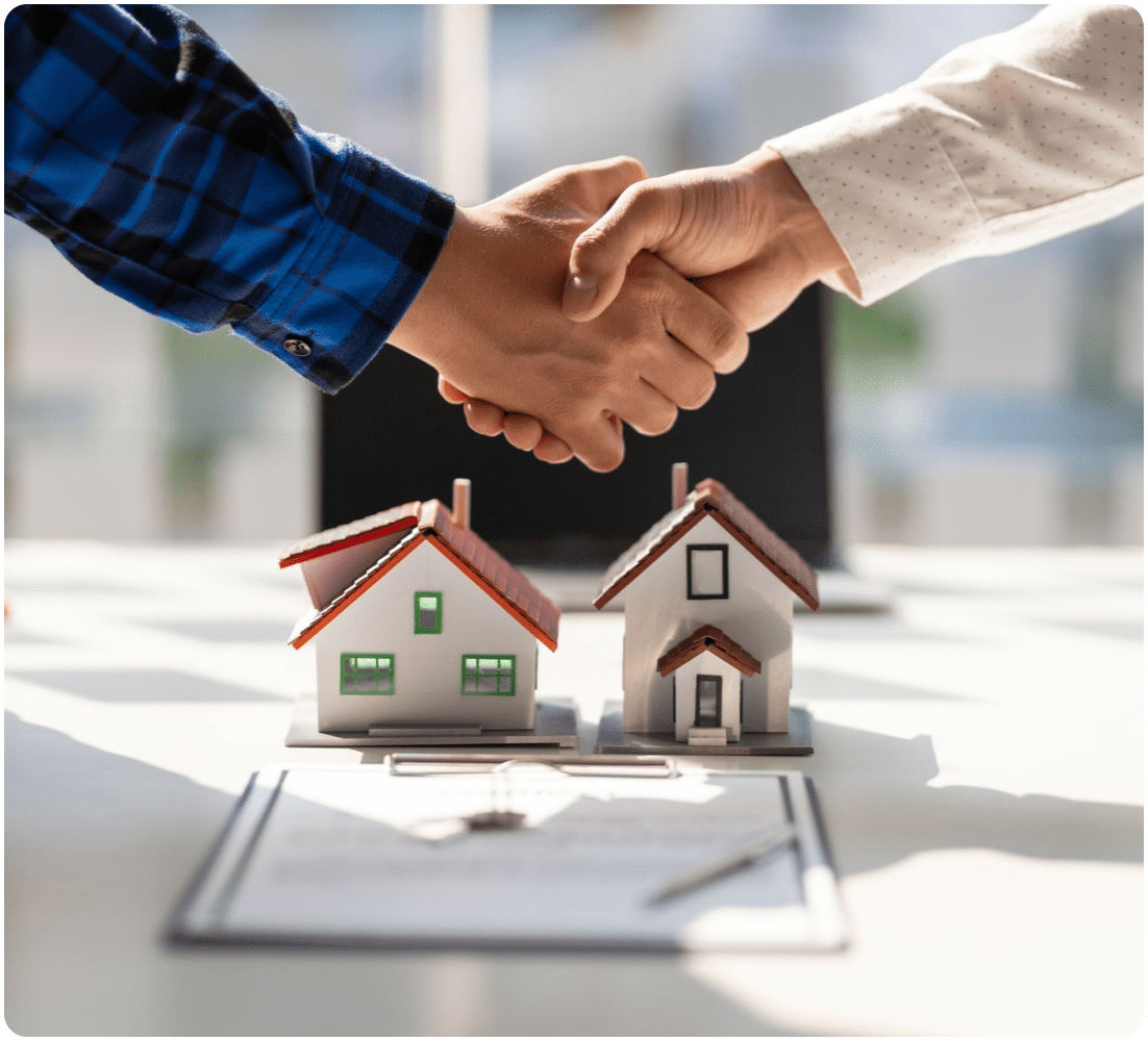 Two people shaking hands over house models.